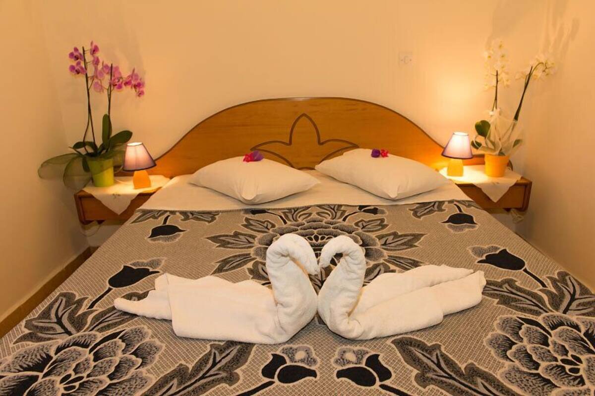 A neatly made bed with two towels arranged in a swan shape, a wooden headboard, and two bedside tables with lamps and potted orchids.