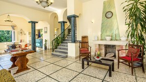 A spacious living area with a fireplace, a staircase, and a large plant. - Alinda Hotel (Leros)