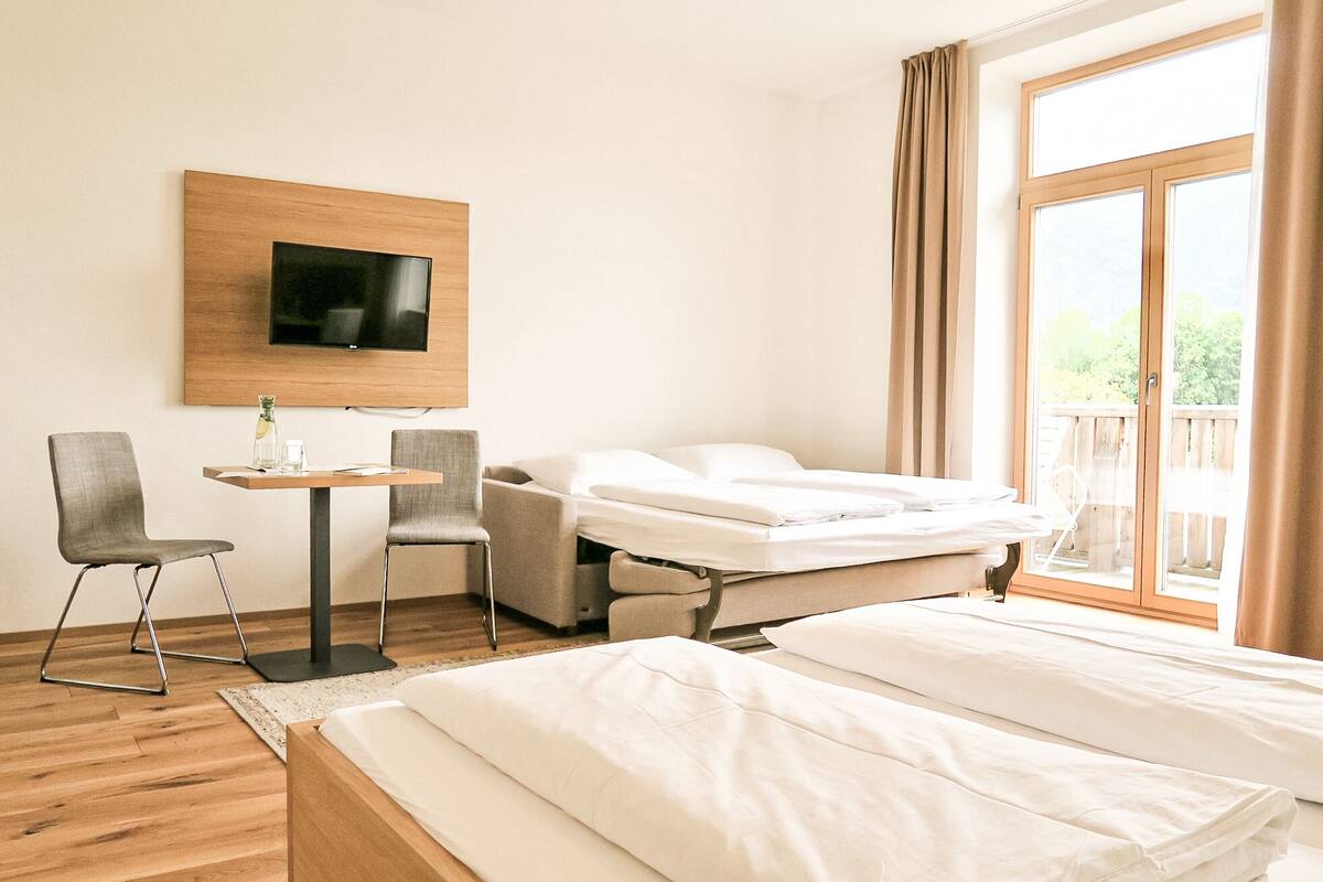 Une chambre d’hôtel comprenant un lit, un bureau avec deux chaises, un téléviseur fixé au mur et une grande fenêtre avec des rideaux.