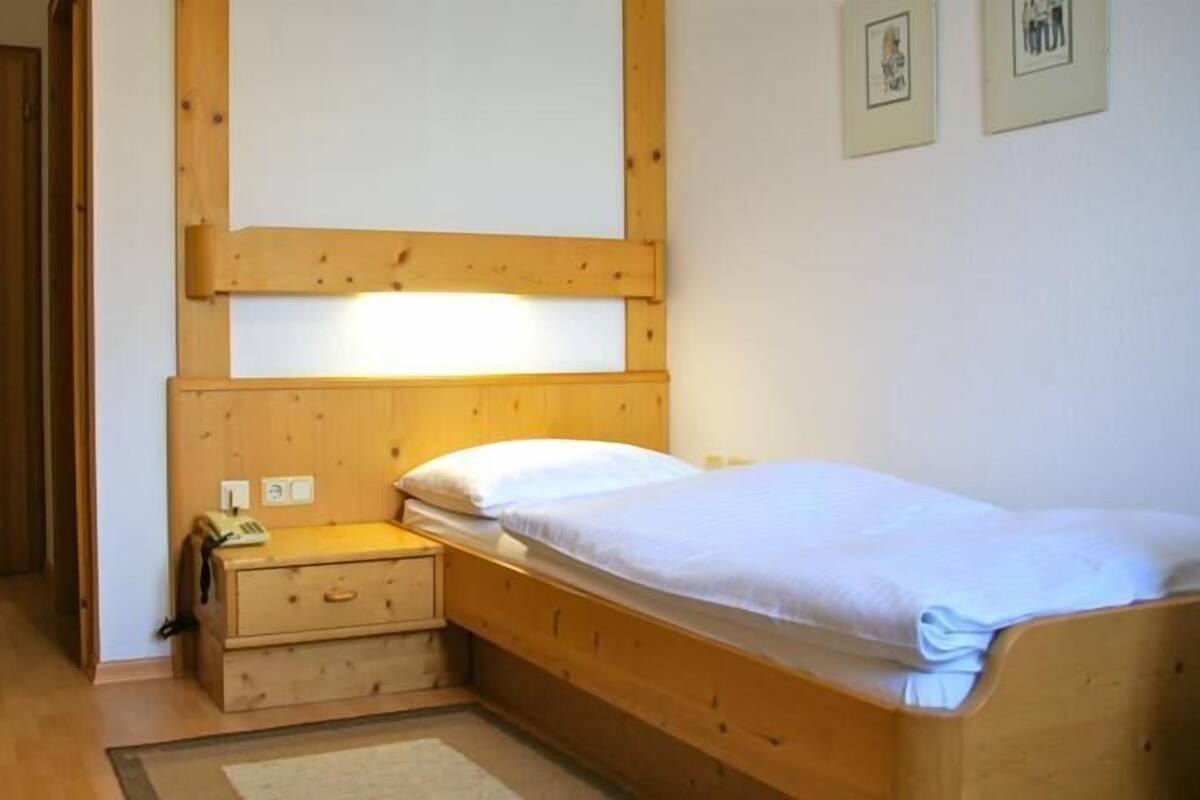 Une petite chambre avec un lit simple, une tête de lit en bois, une table de chevet avec une lampe et une porte.