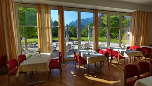 Un restaurante con ventanas amplias, sillas rojas y mesas dispuestas para comer.