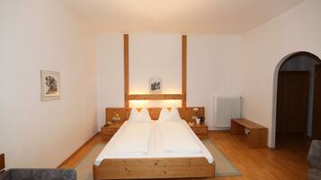 A bedroom with a wooden bed, two bedside tables, a bench, and a radiator.