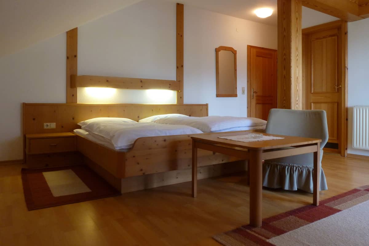Un lit en bois avec une tête de lit, une table de chevet, une chaise et une petite table avec un verre.