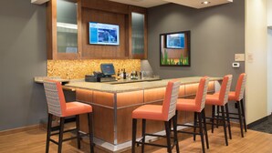 Une cuisine moderne dotée d’un coin bar, comprenant un grand îlot central avec des tabourets de bar, un four encastré et un pare-feu orné d’un motif de mosaïque.