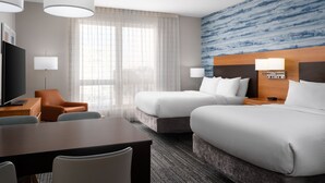 Une chambre d’hôtel avec deux lits, un bureau avec une chaise, une télévision et une grande fenêtre avec des rideaux légers.