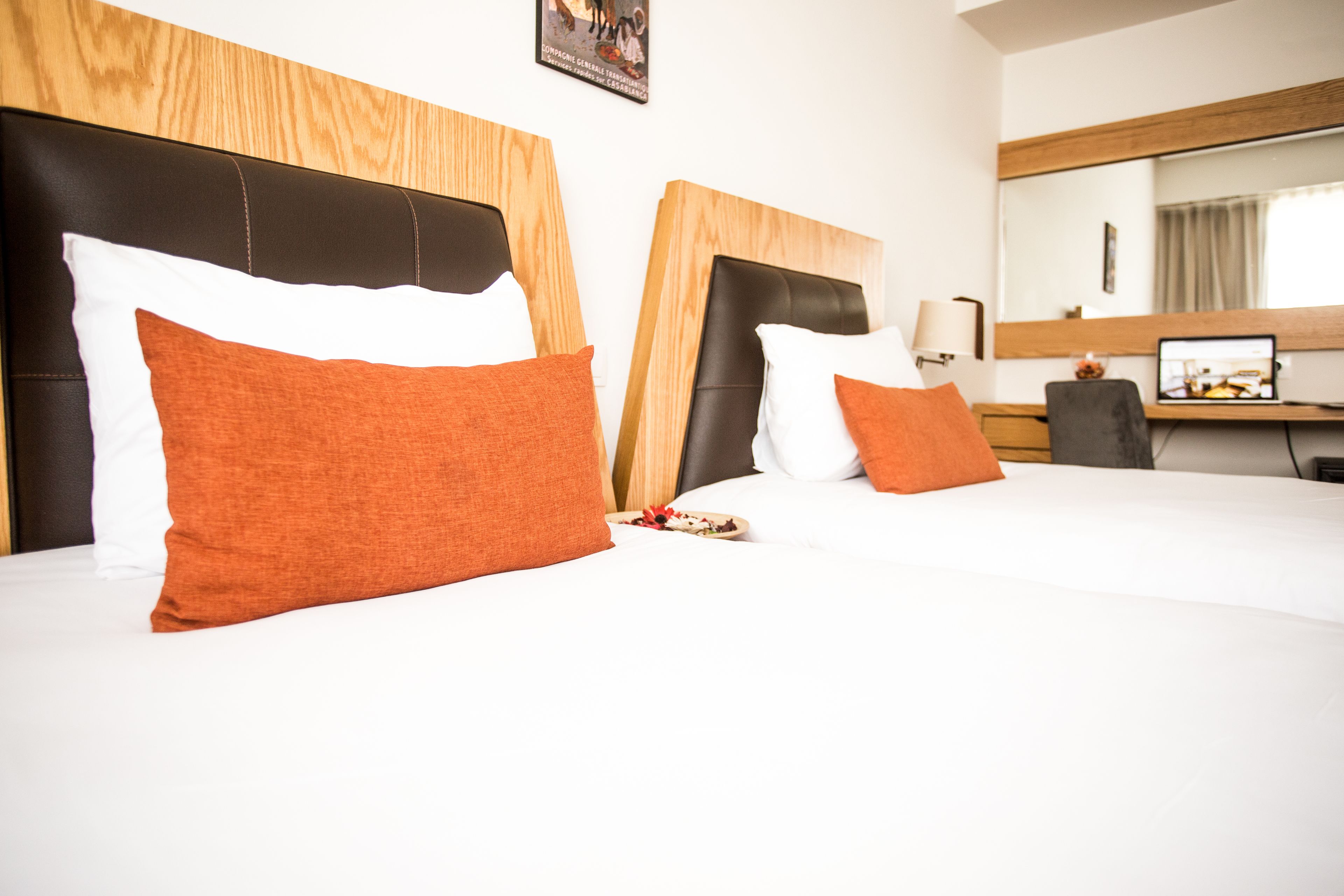Habitación de hotel con dos camas, cada una con cabecero de madera y ropa de cama blanca.