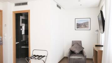 A modern living room with a grey armchair, a small round table, a mounted TV, and a picture on the wall.