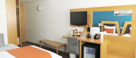 Une chambre d’hôtel avec deux lits, un bureau avec un ordinateur, une télévision et un petit réfrigérateur.