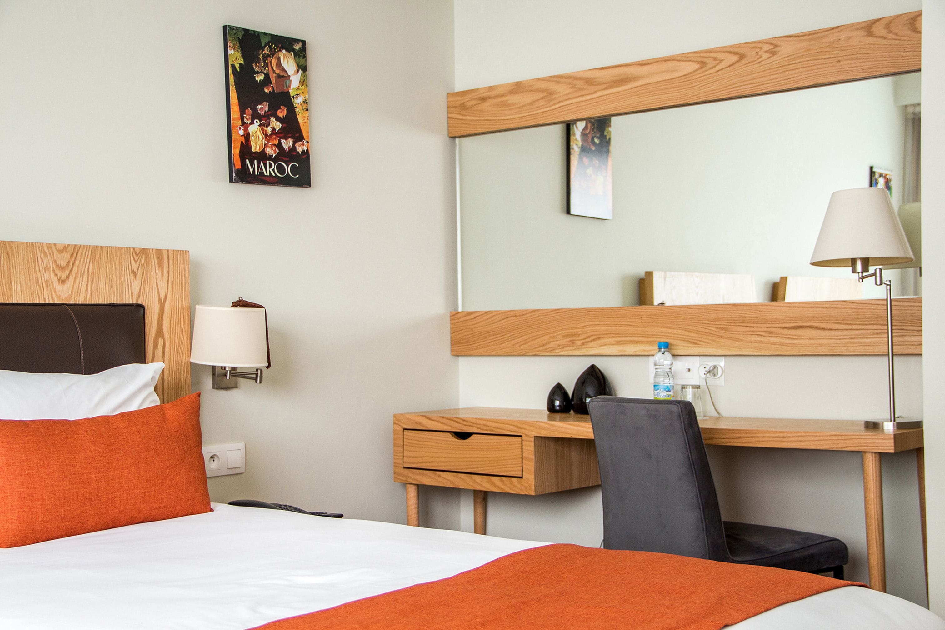 Une chambre d’hôtel avec un lit, un bureau, une chaise, une lampe et un miroir.