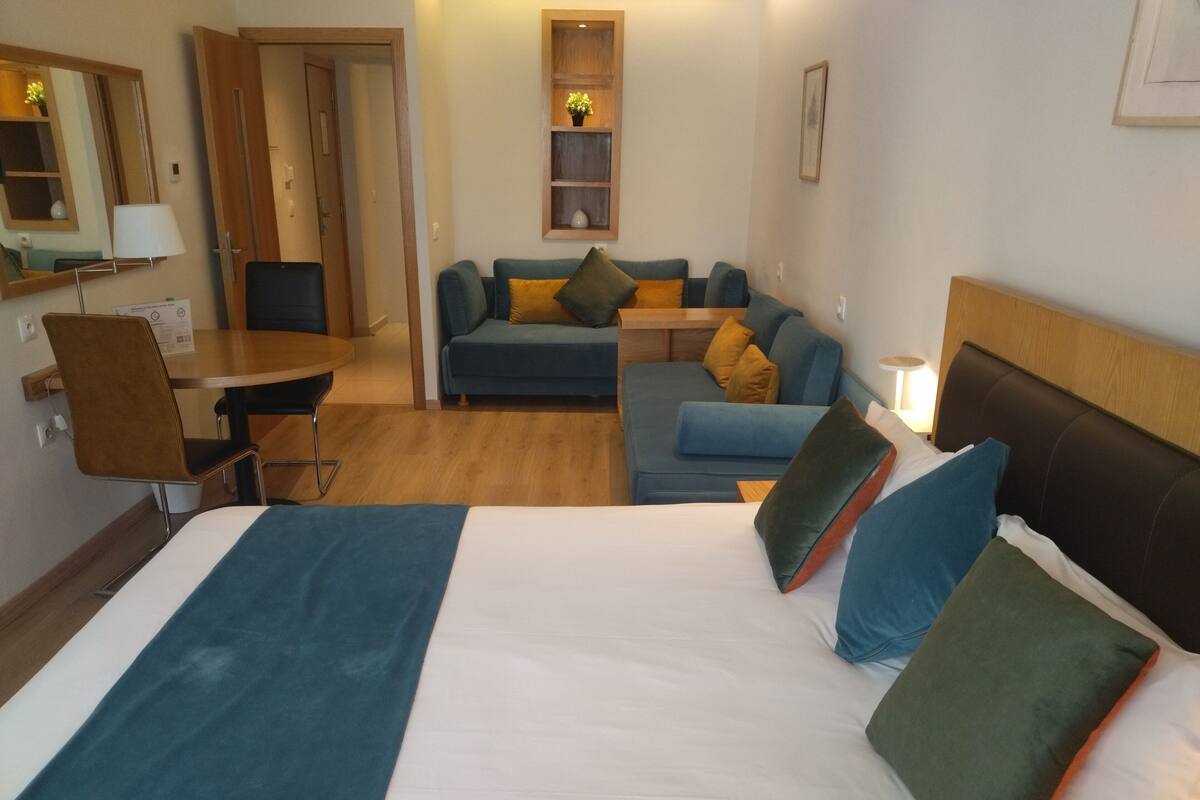 A hotel room with a bed, a sofa, a desk, and a chair.