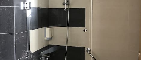 Un baño moderno con cabina de ducha de vidrio, bañera blanca y pared revestida con azulejos negros y beige.