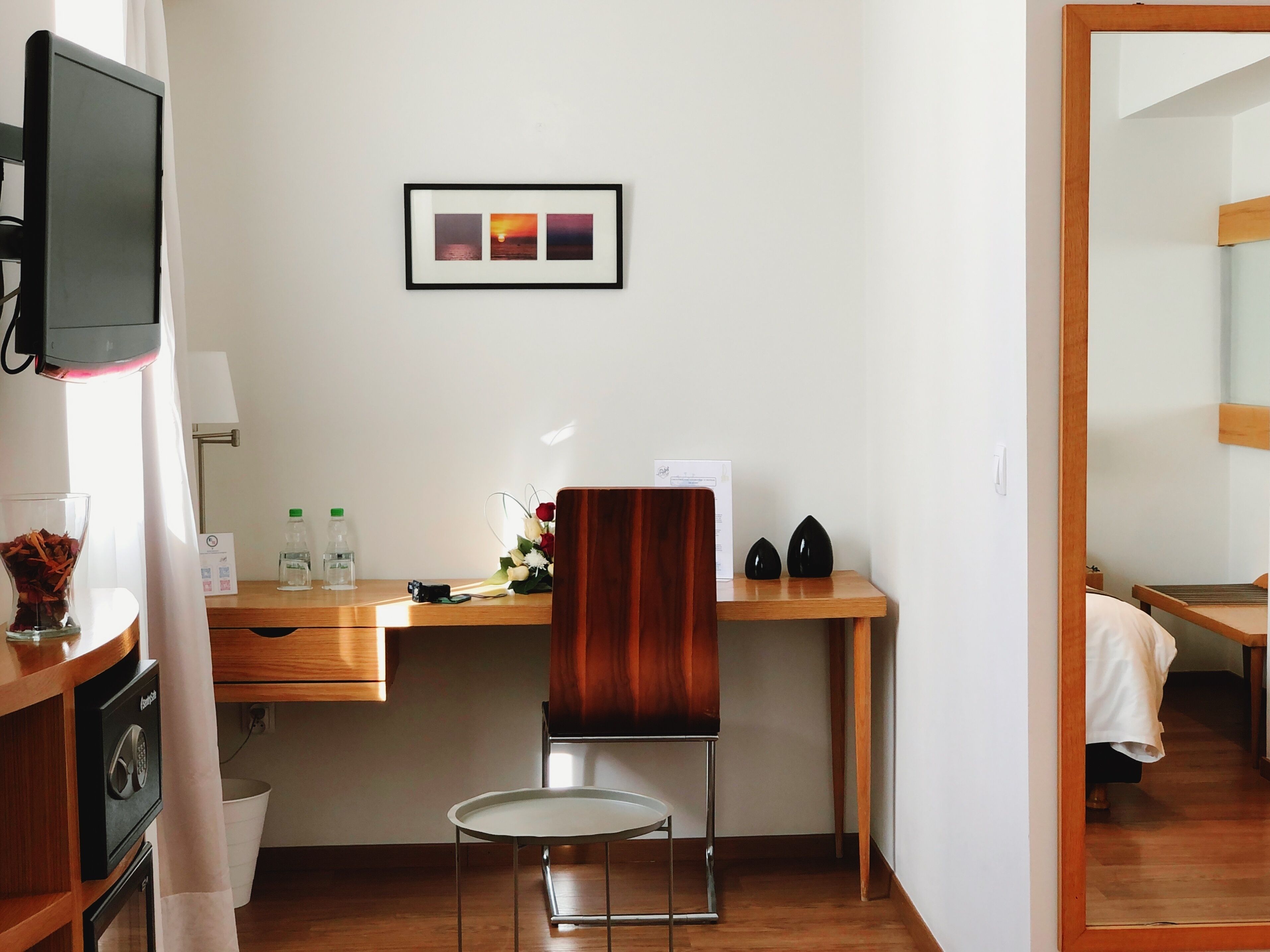 A hotel room with a wooden desk, a chair, a television, and a framed picture on the wall.