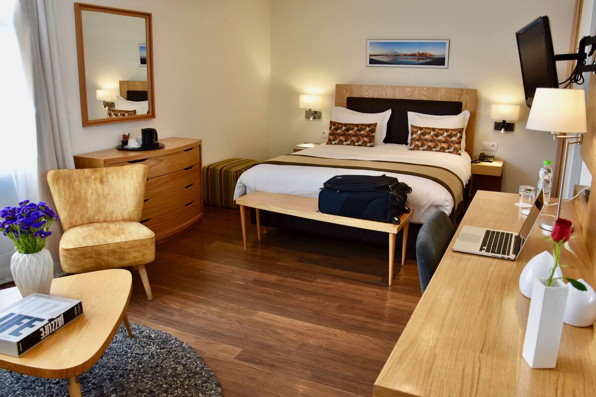 A hotel room with a bed, bedside tables, a desk, a chair, a dresser, a mirror, and a TV.