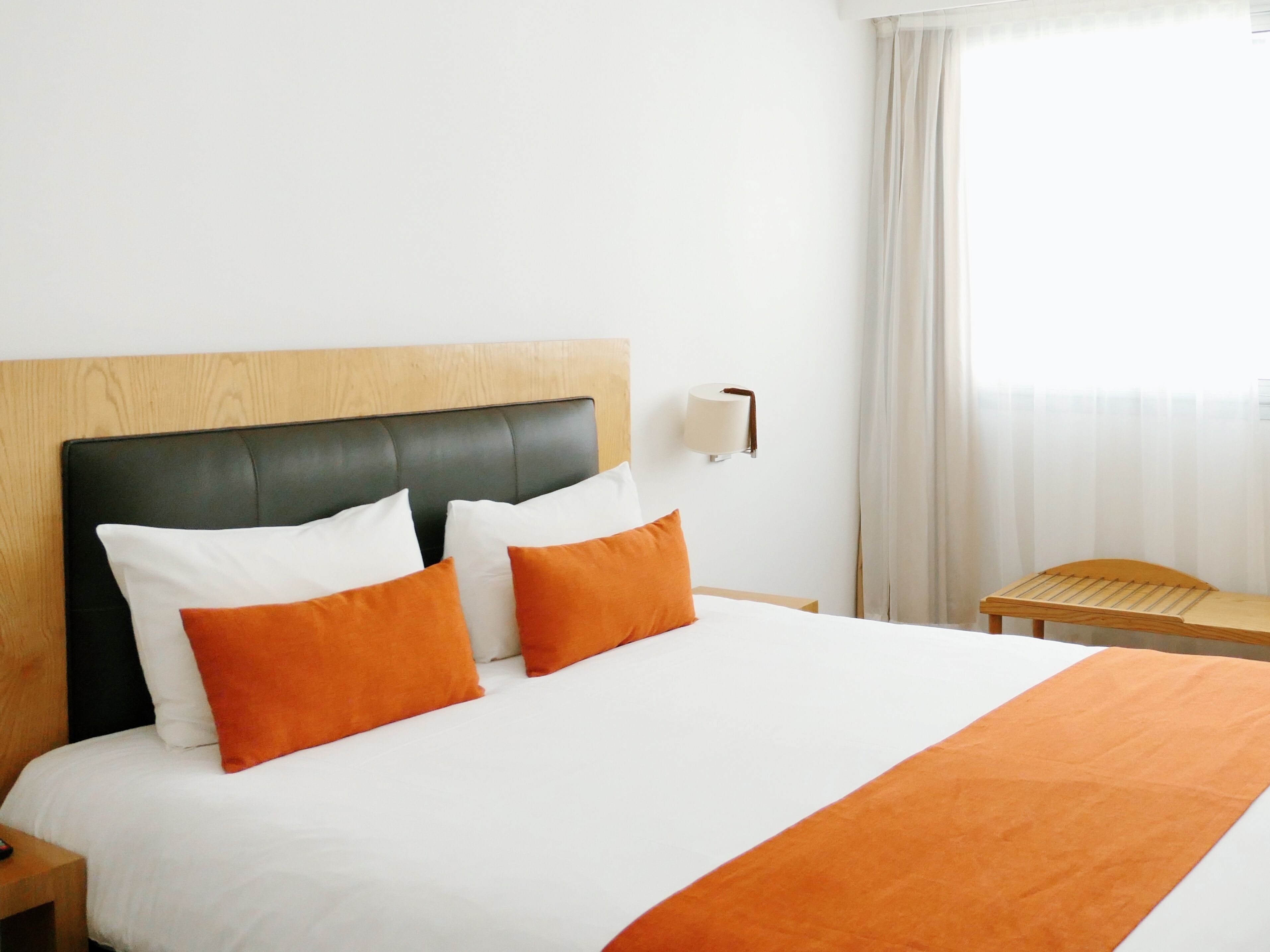 Una habitación de hotel con una cama, una mesita de noche, una lámpara y una ventana con cortinas.