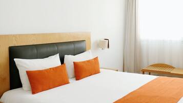 Una habitación de hotel con una cama, una mesita de noche, una lámpara y una ventana con cortinas.