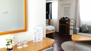 A modern hotel room with a wooden desk, a grey sofa, a TV, and a dining table. - Le Pietri Urban Hotel (Rabat)