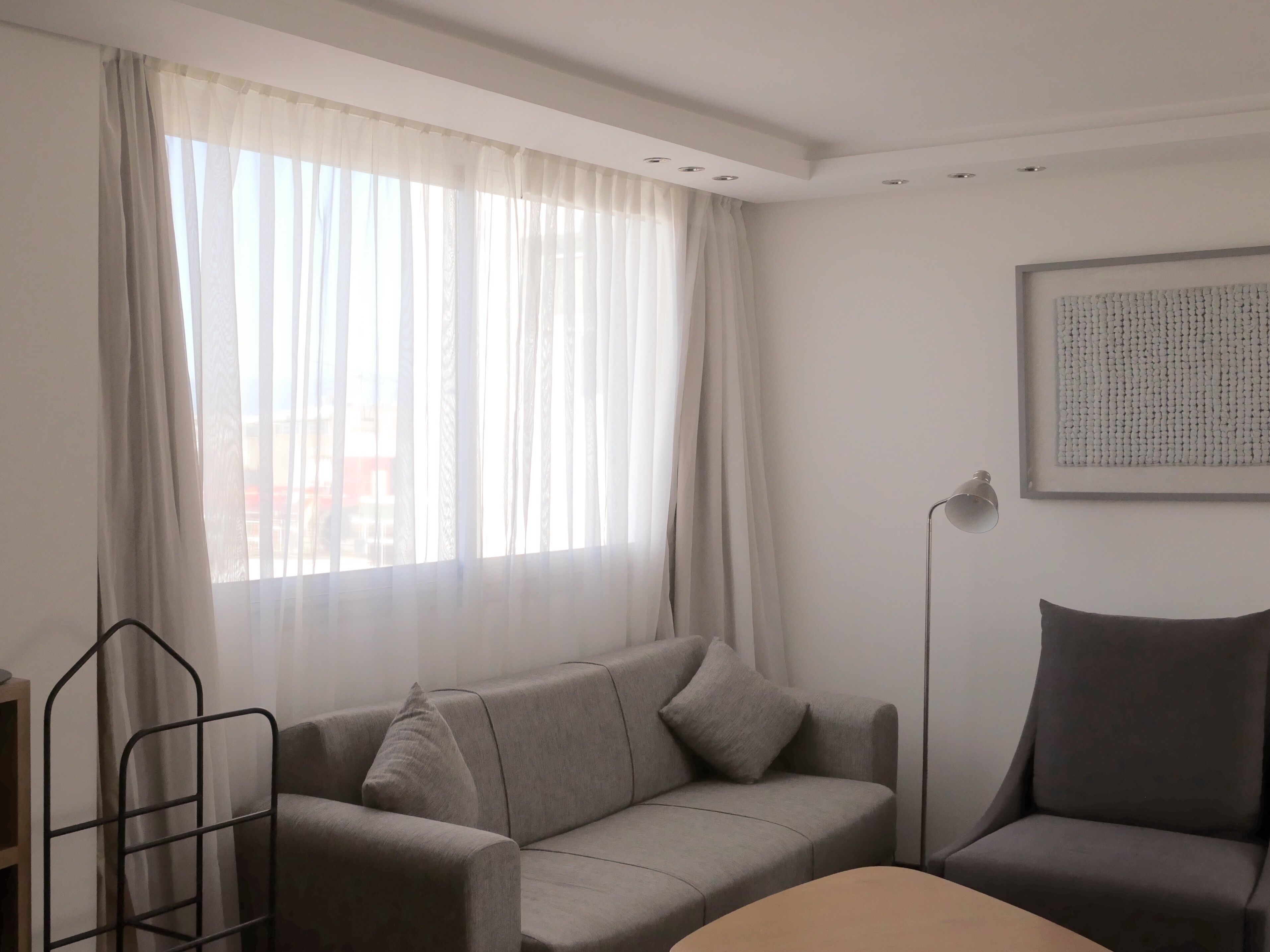 Een moderne, minimalistisch ingerichte kamer met een grijze bank, een klein tafeltje en een vloerlamp.