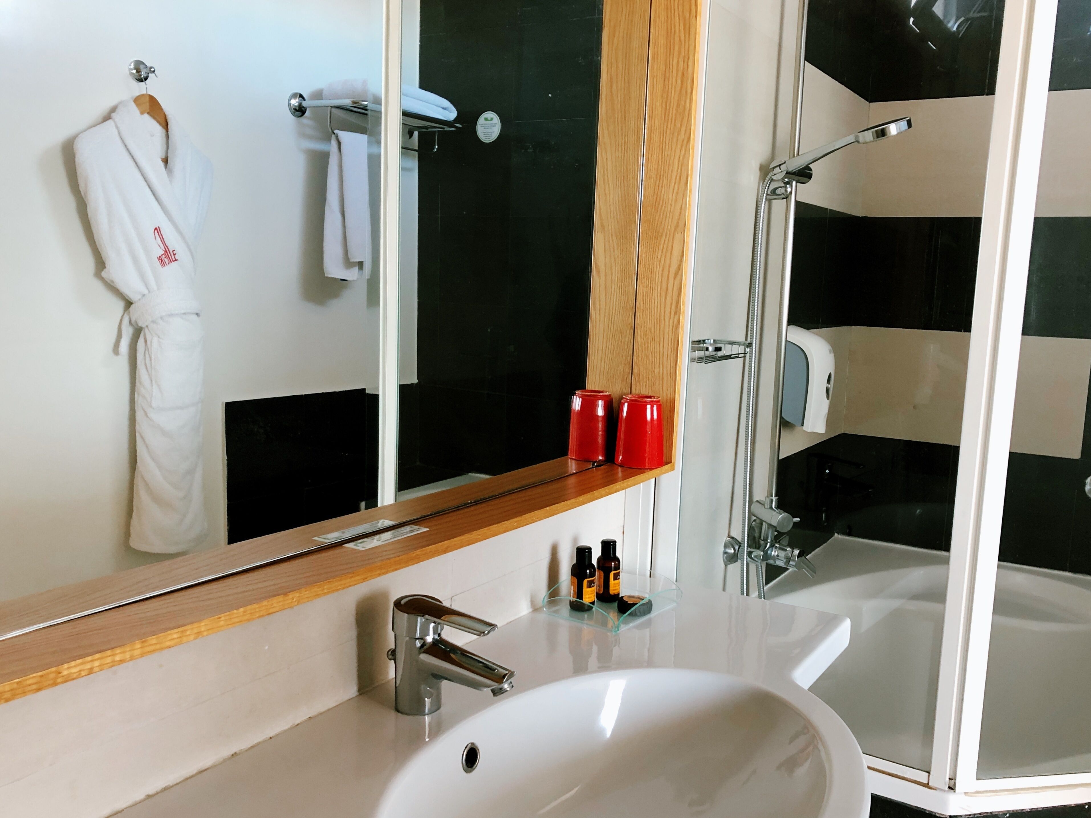 A bathroom with a white sink, a mirror, a robe hanging on a rack, and a shower area.