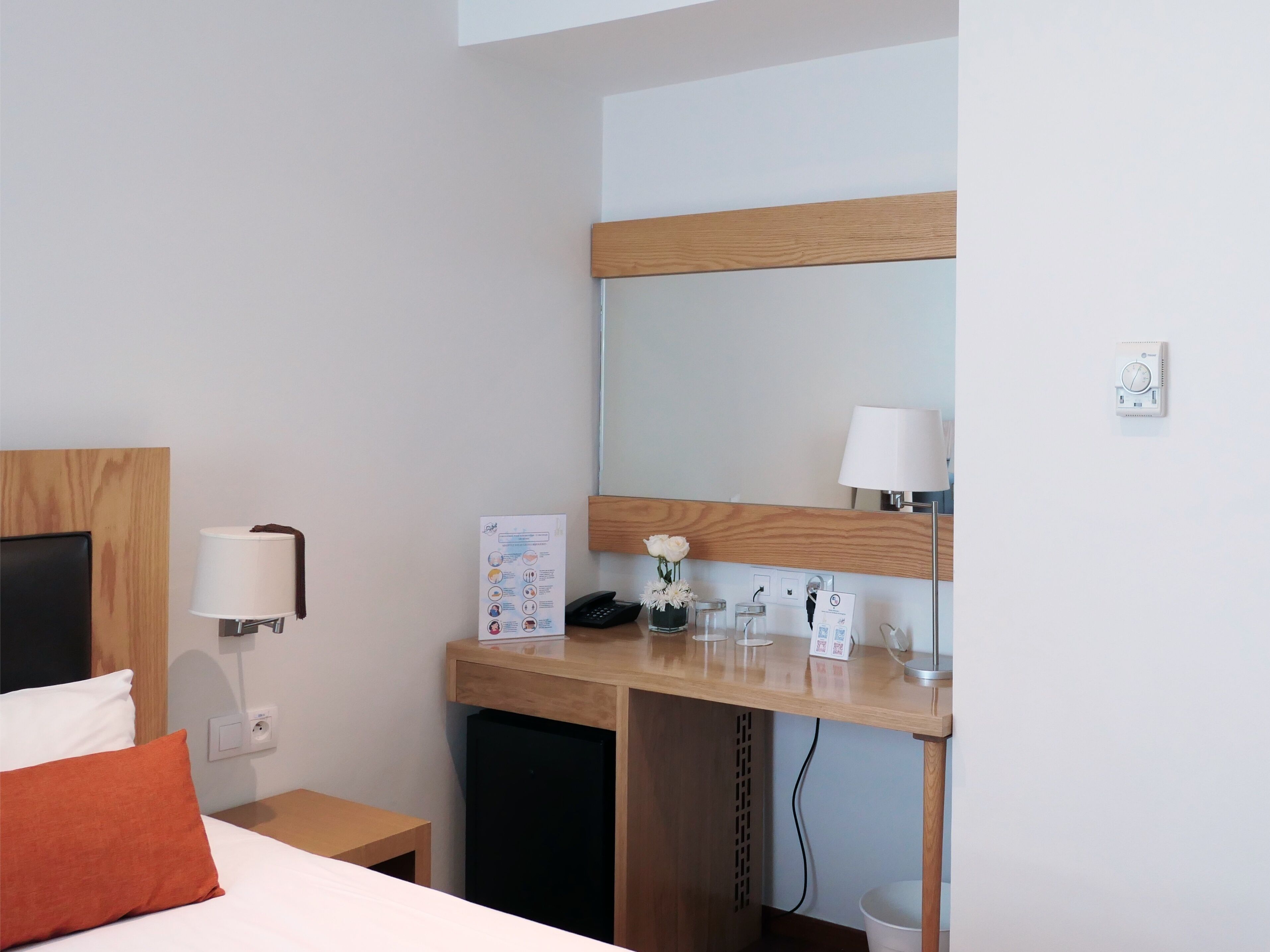 Hotelkamer met een bed, een bureau met spiegel, een lamp, een telefoon, een klein tafeltje en een prullenbak.