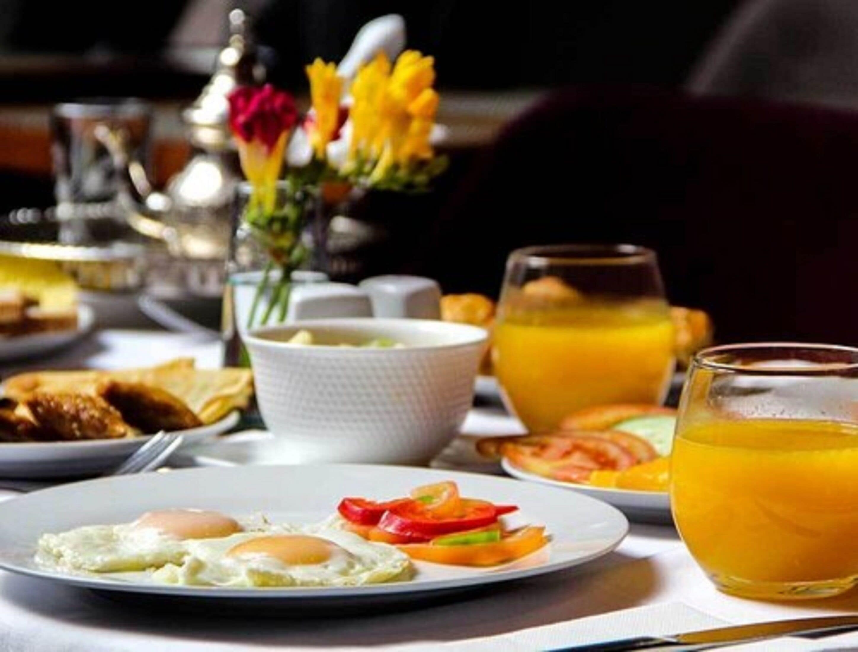 Une table dressée pour le petit-déjeuner, avec des œufs, des légumes et du jus d’orange.
