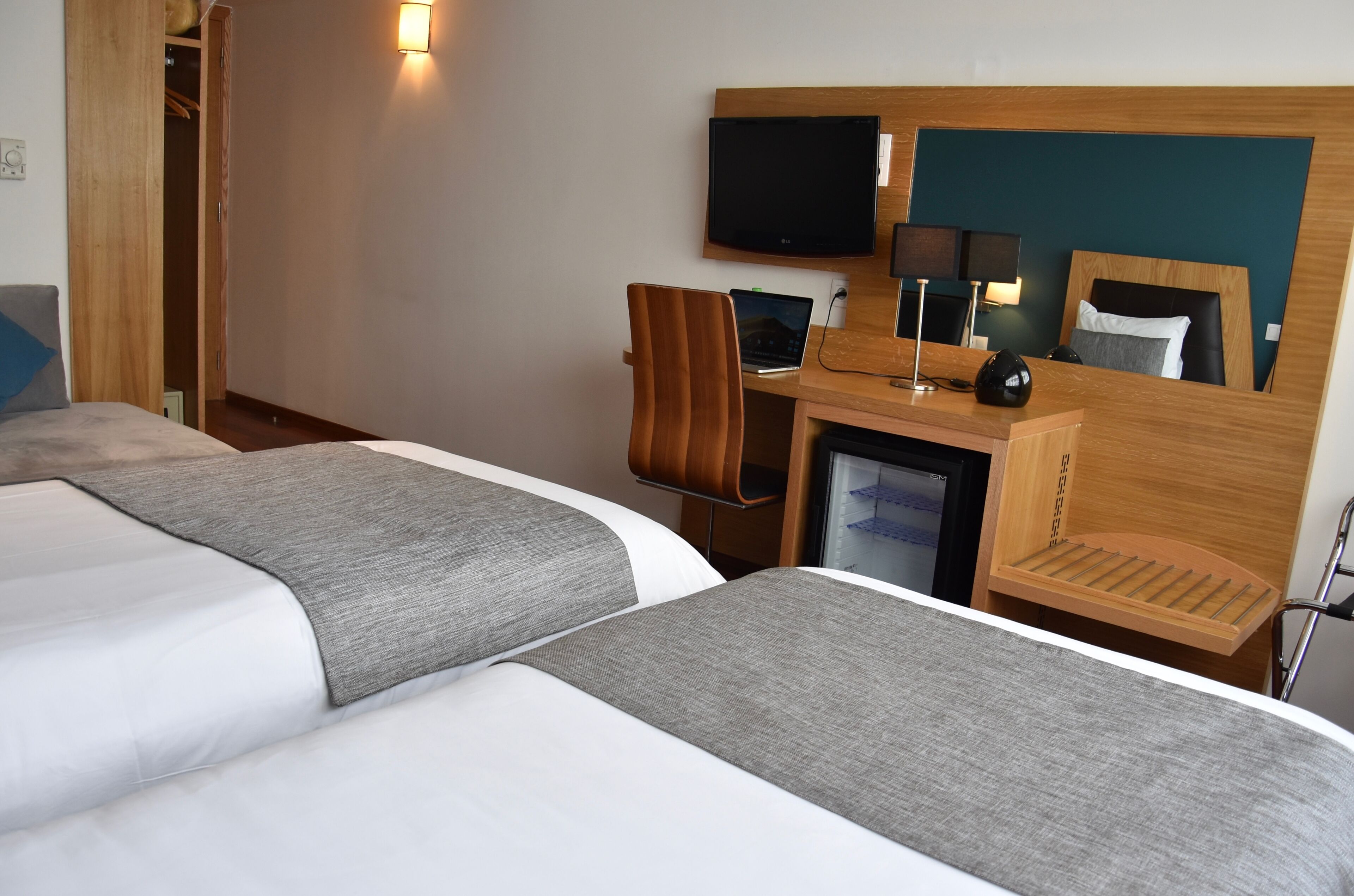 Habitación de hotel con dos camas, un escritorio con una computadora portátil, un televisor y un refrigerador pequeño.