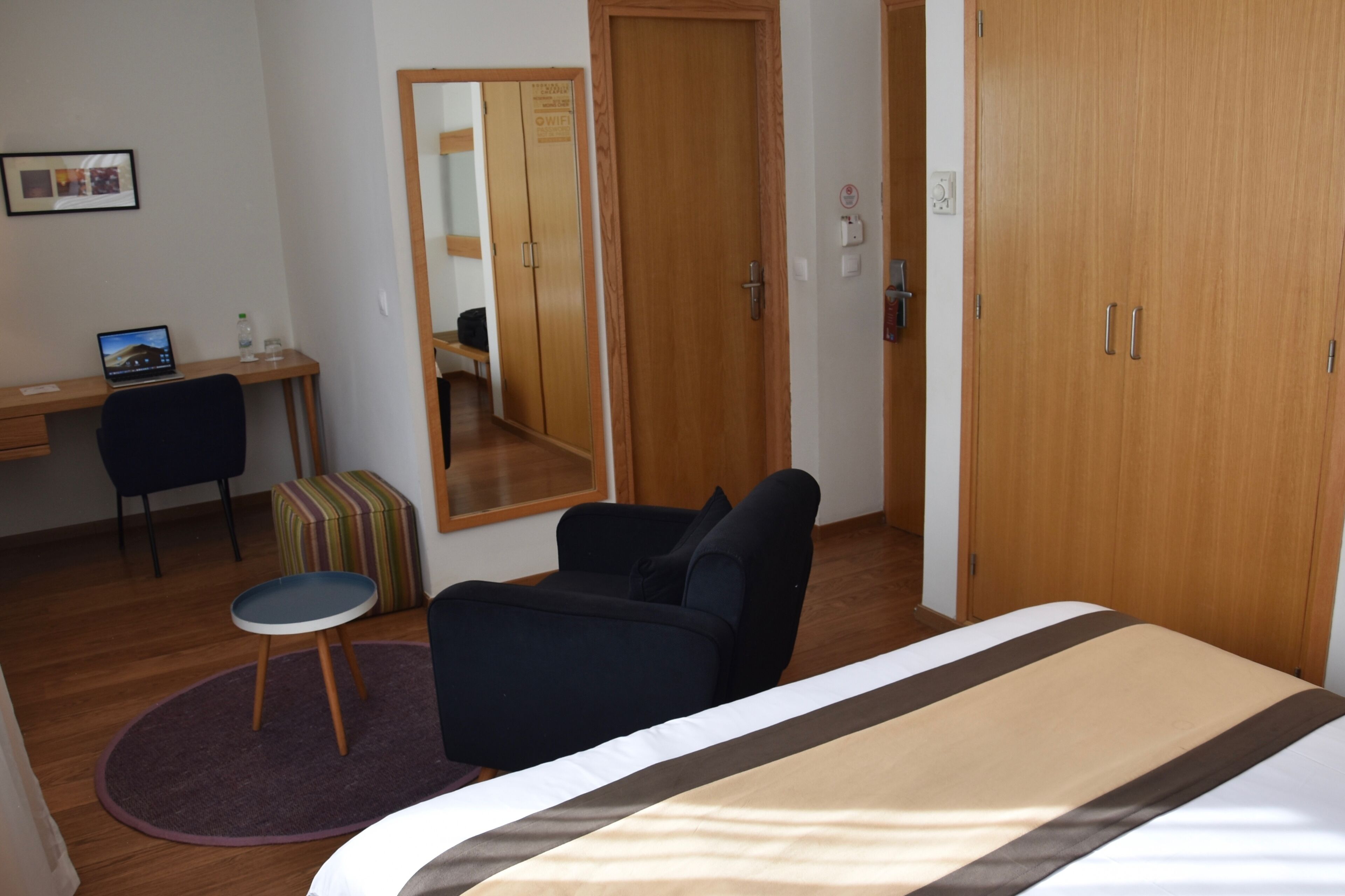 Une chambre d’hôtel avec un lit, un bureau avec un ordinateur portable, une chaise, une petite table ronde et un miroir.