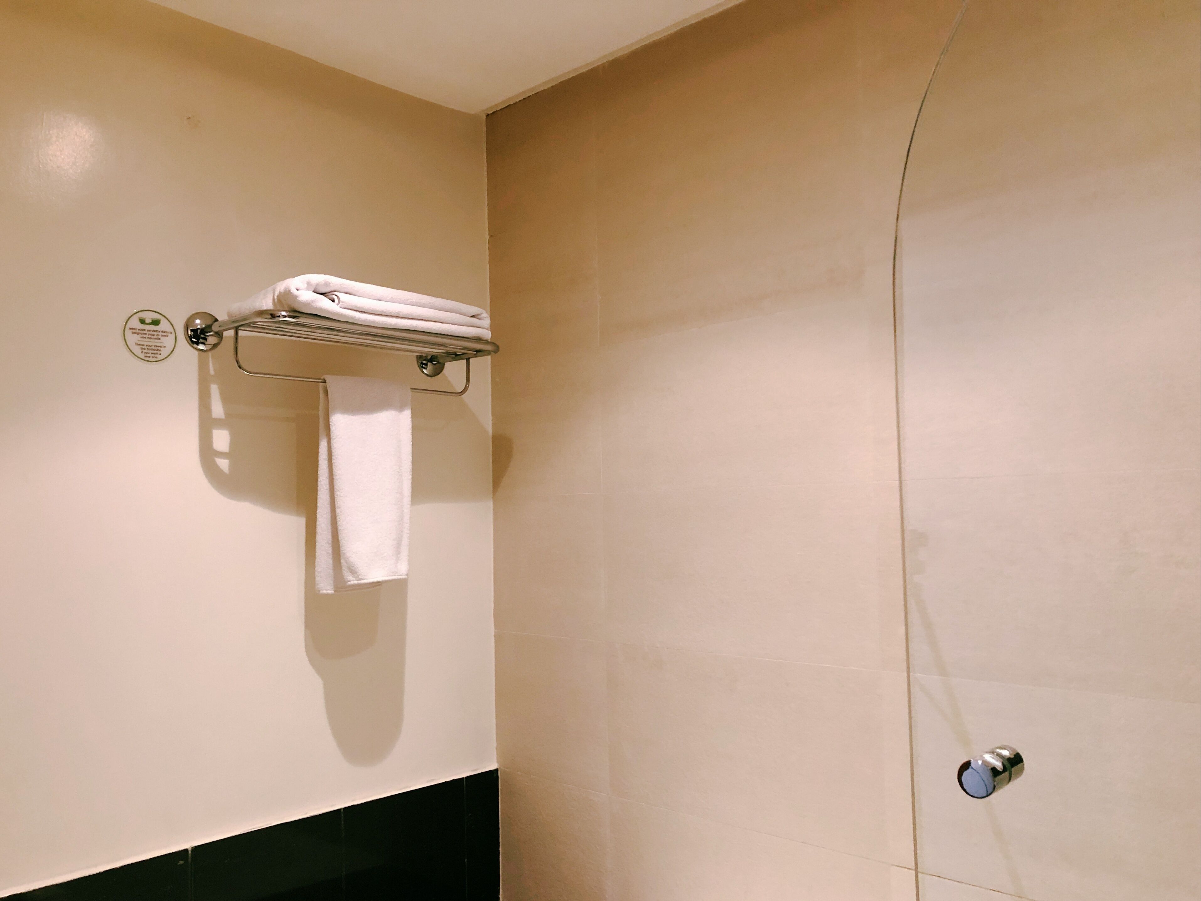 Un baño con un perchero que sostiene dos toallas, un letrero en la pared y una puerta con manija.