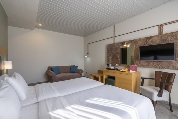 A hotel room with a large bed, a desk, a chair, a TV, and a mirror.