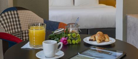 Ein Frühstückstisch mit Tasse, Orangensaftglas, Croissant und Tablet, das eine Seite zur Hotelzimmerbuchung anzeigt.
