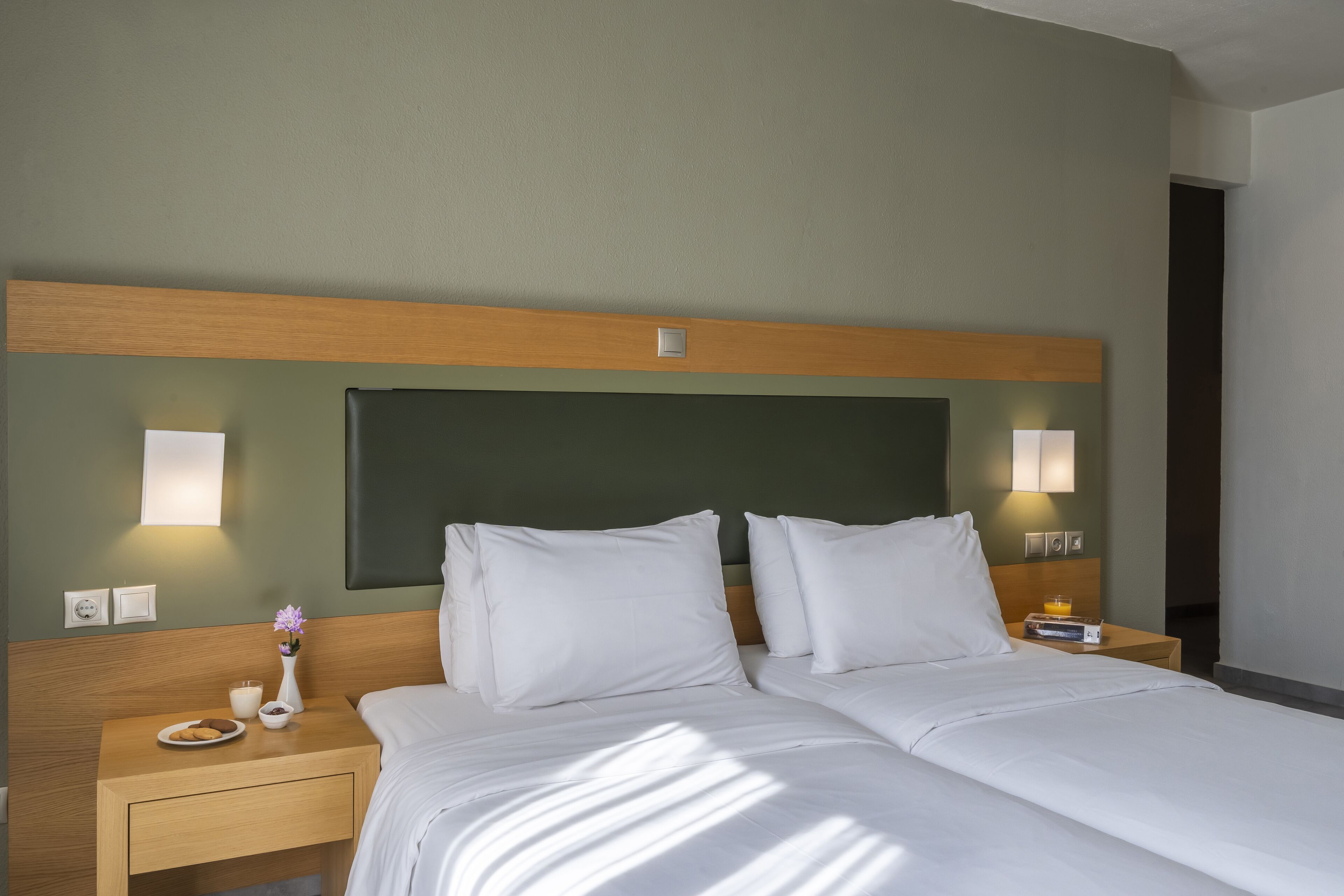 A hotel room with a large bed, two bedside tables, a nightstand, and a wall-mounted light fixture.