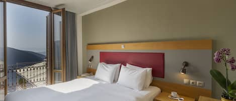 A hotel room with a bed, bedside table, and a view of the mountains through the balcony.