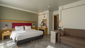 A modern hotel room with a large bed, a sofa, a desk, and a mirror.