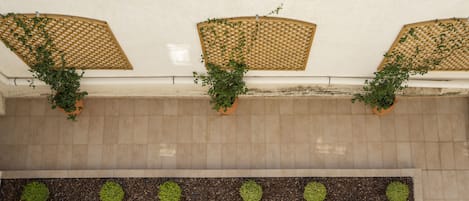 A rooftop terrace with terracotta tiles, three wooden lattice planters with green plants, and a low wall with evenly spaced green shrubs.