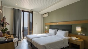 A hotel room with two beds, a desk with a laptop, a plant, and a view of the outdoors. - Kastalia Boutique Hotel (Delphi)