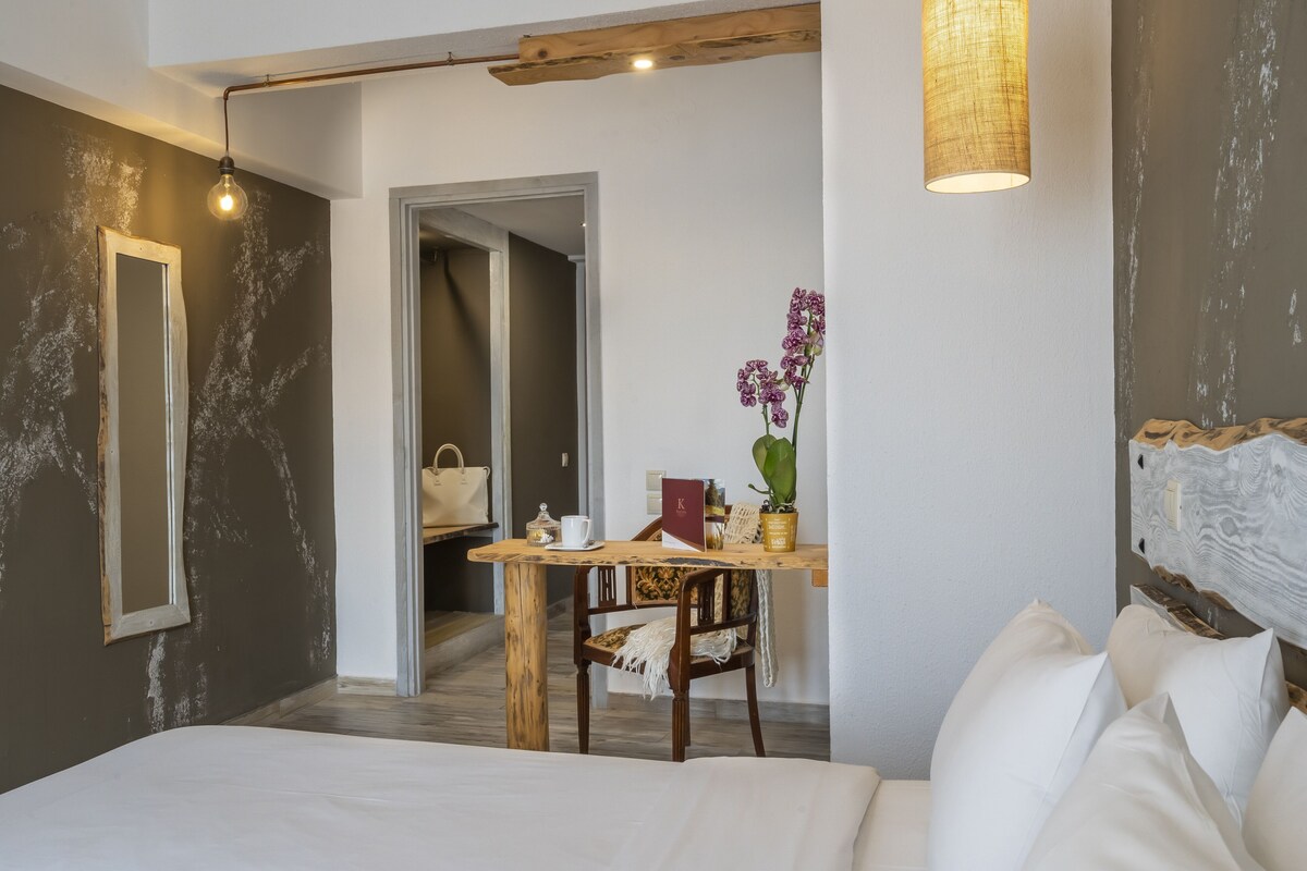 A bedroom with a bed, a wooden desk, a chair, a mirror, and a hanging light fixture.