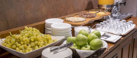 A buffet with plates of grapes, apples, and a variety of other foods.