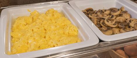 A buffet with scrambled eggs and sliced mushrooms.