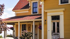 A yellow house with a red roof, a porch with columns, and a sign that reads 'GUESTHOUSE.' - Magnetic Hill Winery (Moncton)