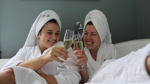 Two individuals in white robes toasting with champagne glasses in a room with a framed picture on the wall. - Magnetic Hill Winery (Moncton)