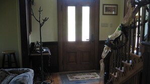 A room with wooden flooring, a wooden door, a staircase, a chair, a table, and a coat rack. - Magnetic Hill Winery (Moncton)