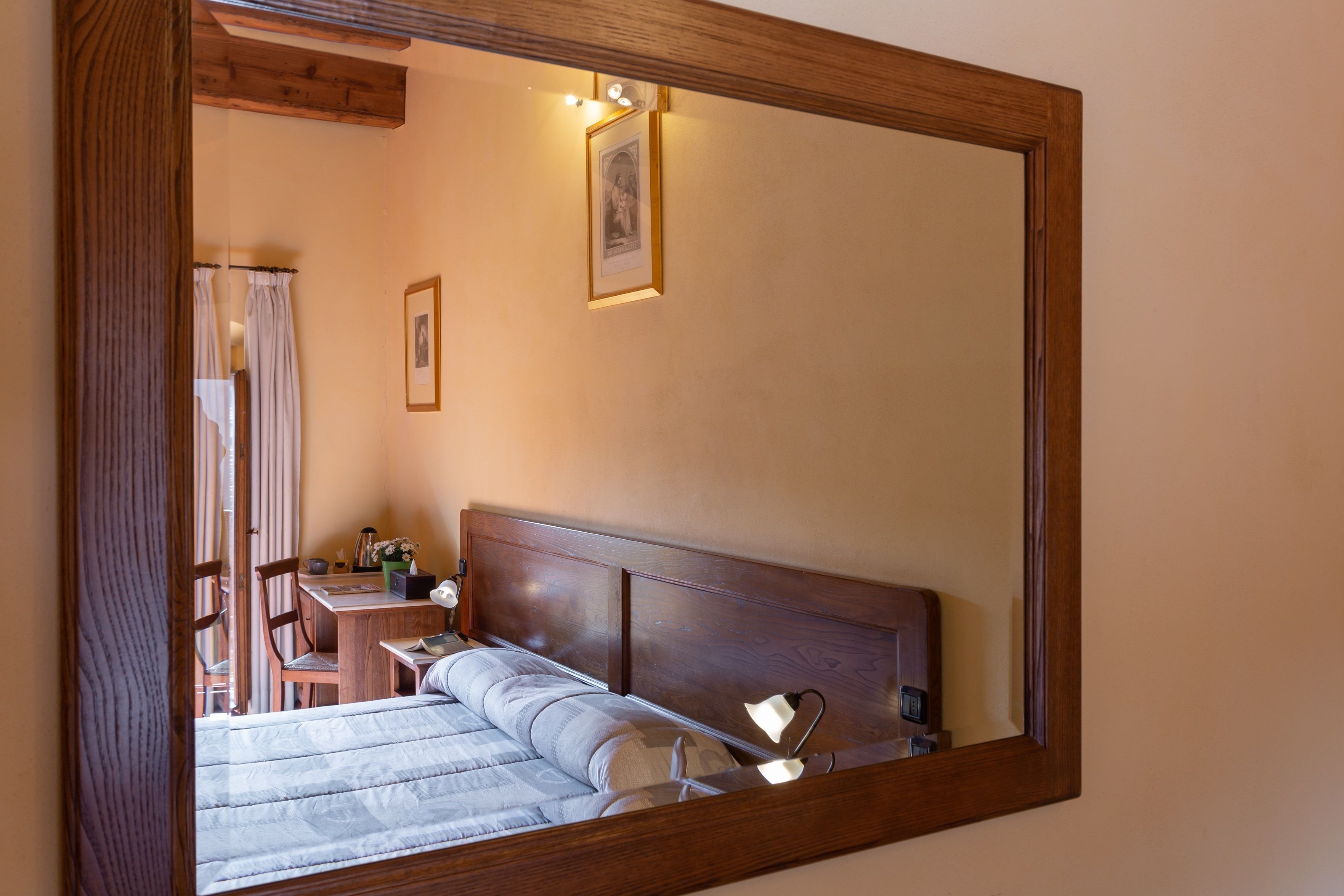 Une chambre à coucher avec une tête de lit en bois, un lit recouvert d’une courtepointe, une table de chevet, une chaise et un miroir qui reflète la pièce.