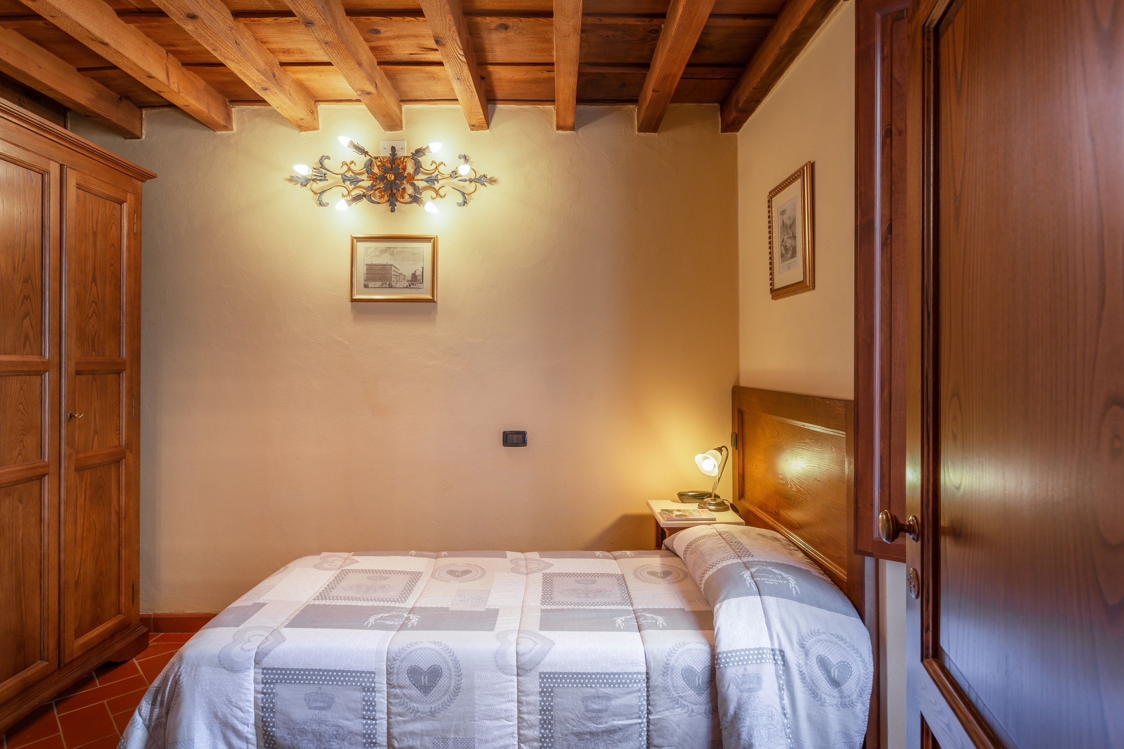 Ein Schlafzimmer mit Holzboden, einem Bett mit gemustertem Überwurf, einem Nachttisch mit Lampe und einem Holzschrank.