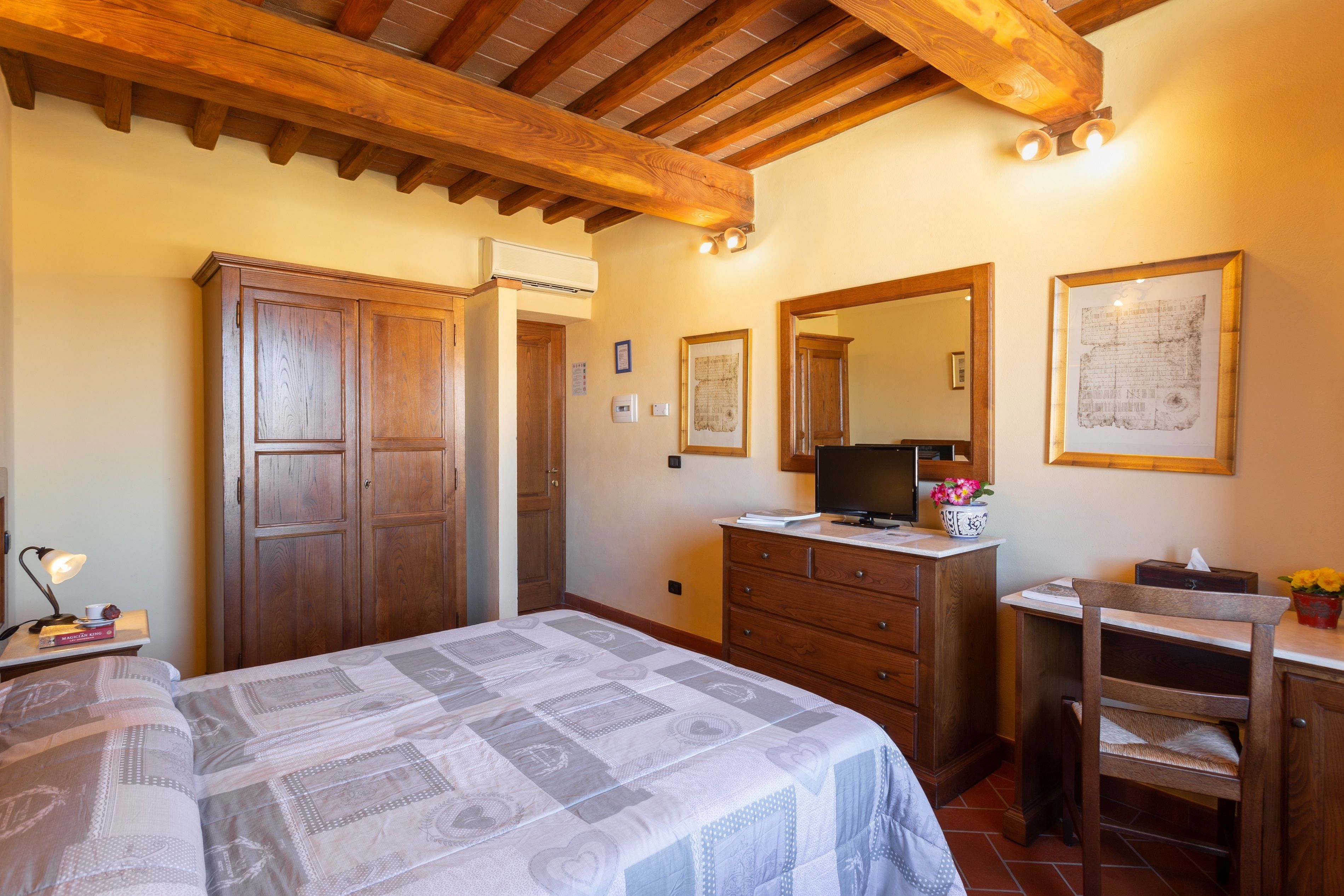 A bedroom with a bed, wooden wardrobe, dresser, and a desk with a mirror and a map on the wall.
