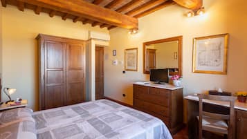 A bedroom with a bed, wooden wardrobe, dresser, and a desk with a mirror and a map on the wall.