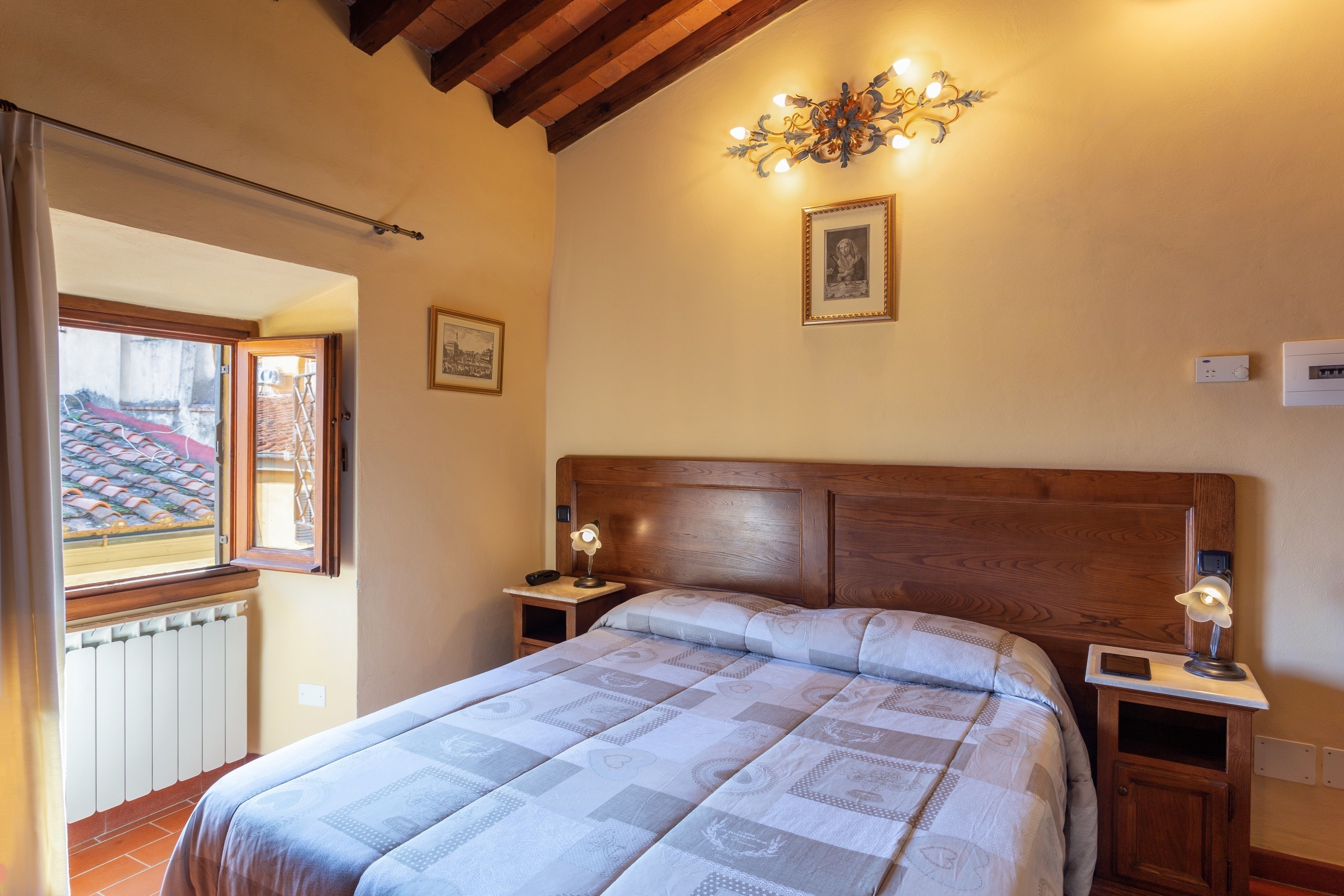 A bedroom with a wooden headboard, a quilted bedspread, bedside tables with lamps, and a wall-mounted light fixture.