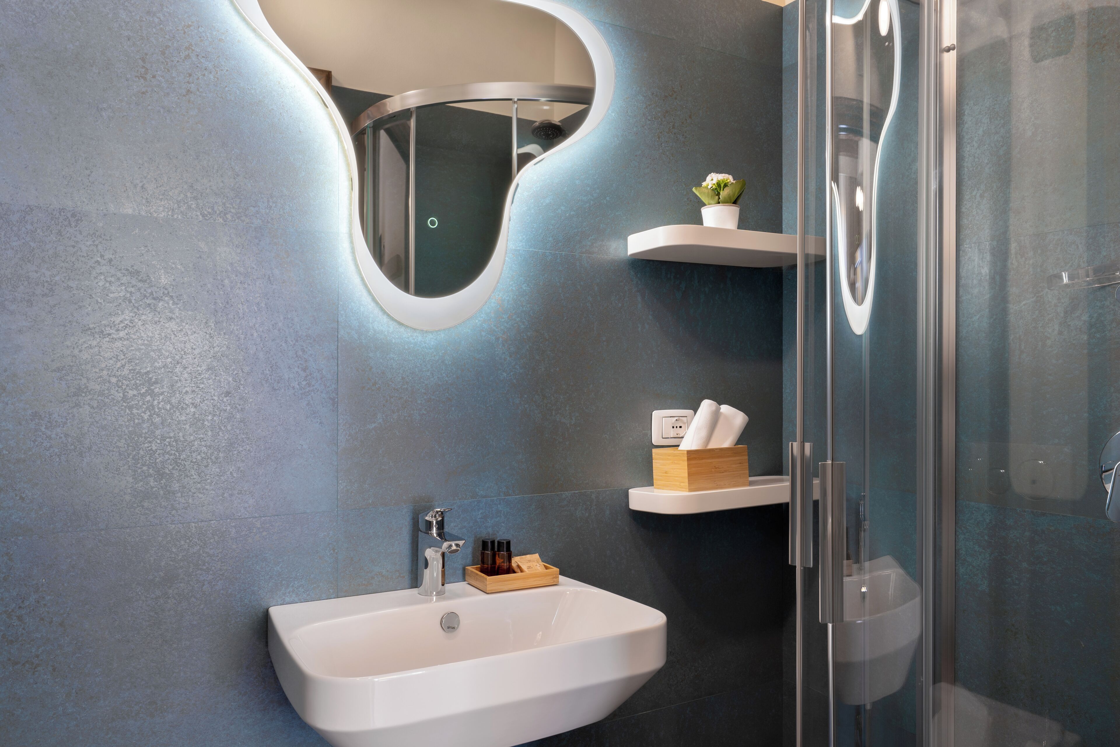 A modern bathroom with a white sink, a glass shower enclosure, and a mirror with a unique curved design.