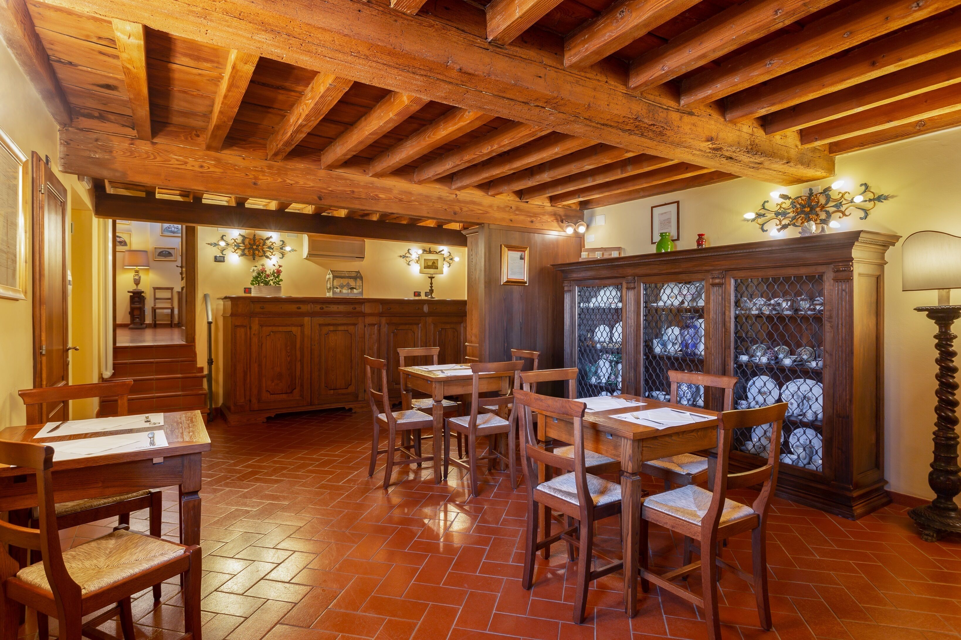 Ein Essbereich mit Holztischen und -stühlen, im Hintergrund eine Küche und ein dekorativer Schrank mit Glastüren.