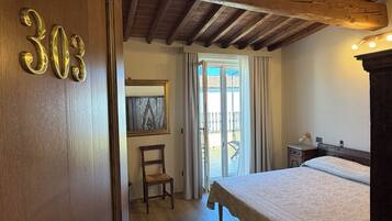 Une pièce avec un lit, une chaise, une porte en bois portant des numéros, et une vue par la fenêtre.