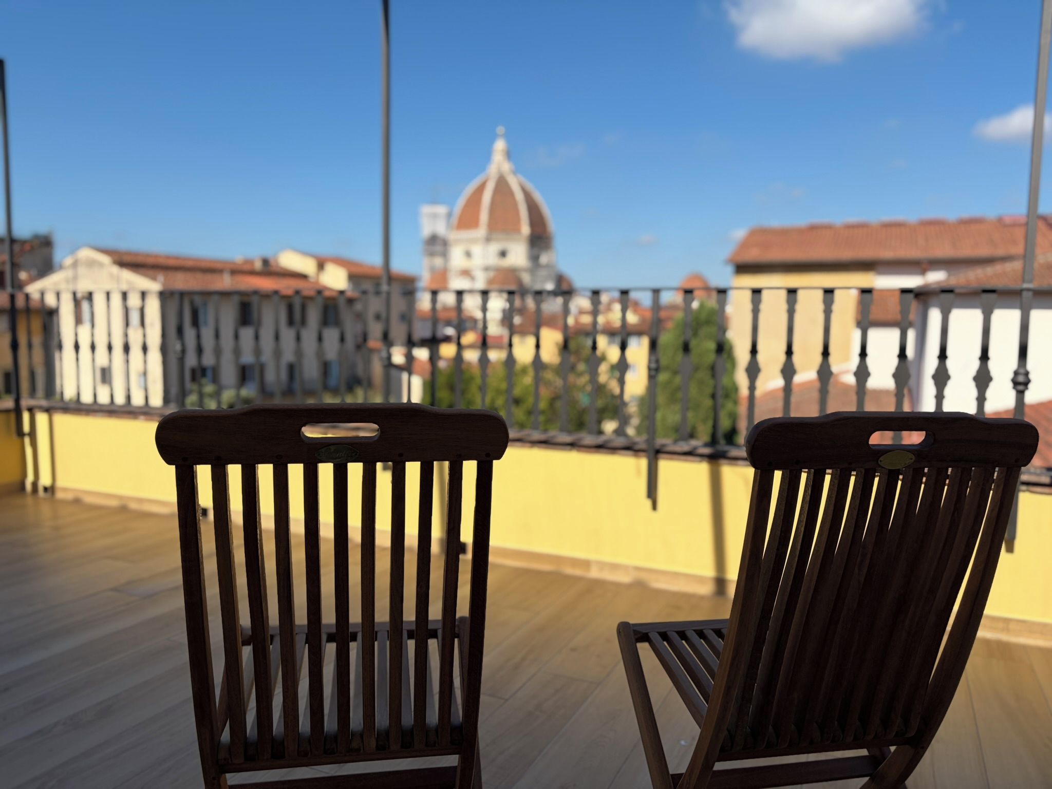 Two wooden chairs on a balcony with a view of a domed building and cityscape.