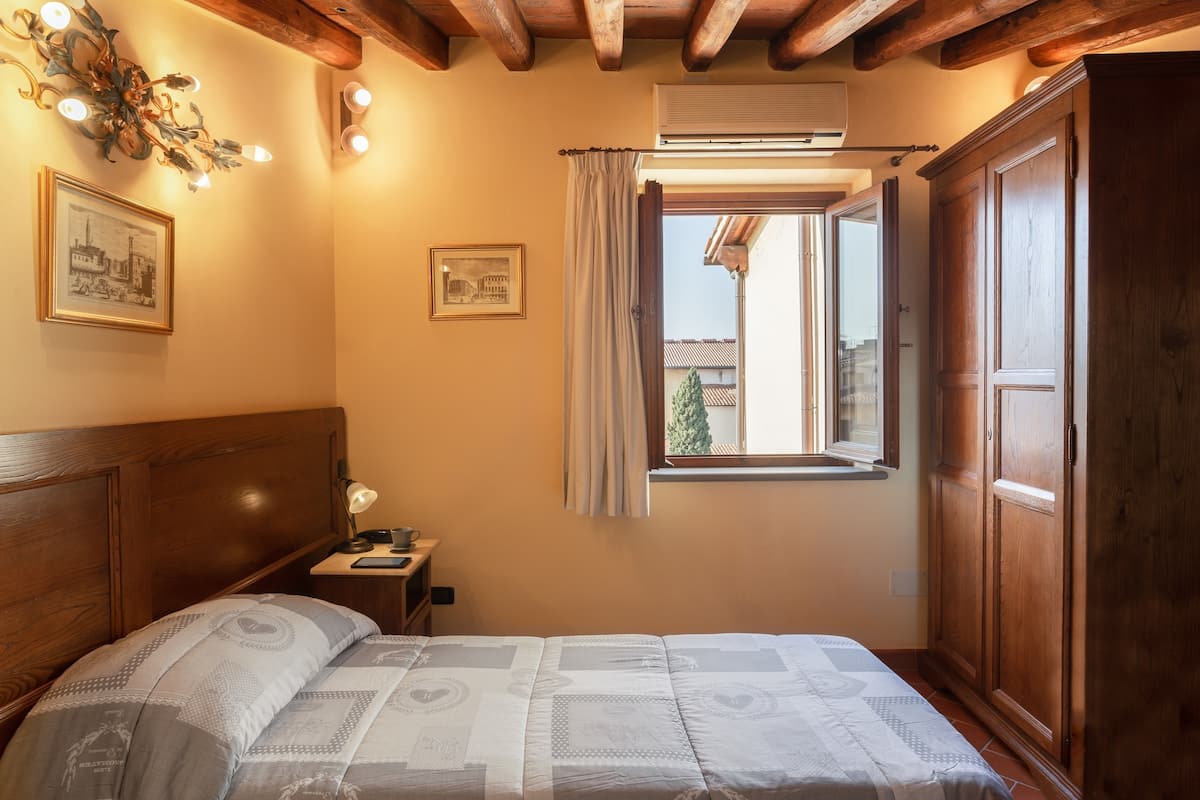 Een slaapkamer met een houten hoofdbord, een bed met beddengoed met een patroon, een nachtkastje met een lamp en een raam met gordijnen.